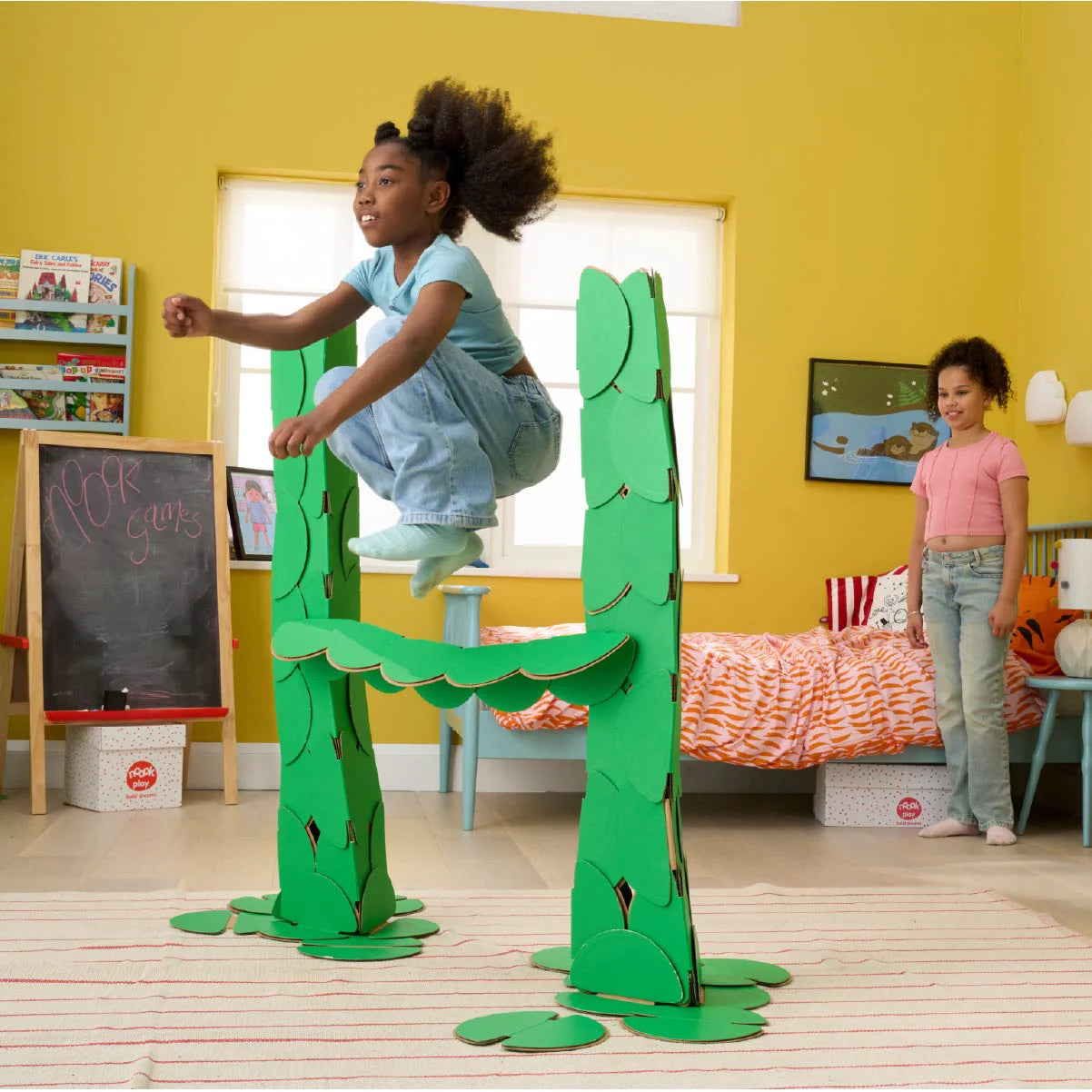 Two girls are playing in a bedroom, jumping over hurdles made out of a noook play® building kit.
