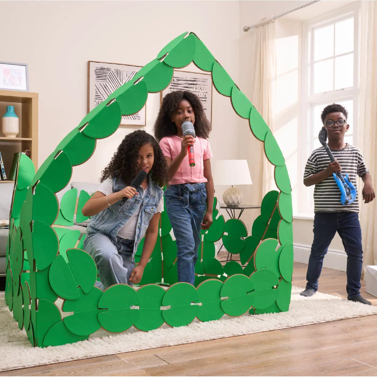 Three kids are playing in a sitting room, pretending to be pop singers on a concert stage made out of noook play® building kits. The girls are singing into microphones and the boy is strumming a blue inflatable guitar.
This Pop Stage took 85 noook play® discs to build.