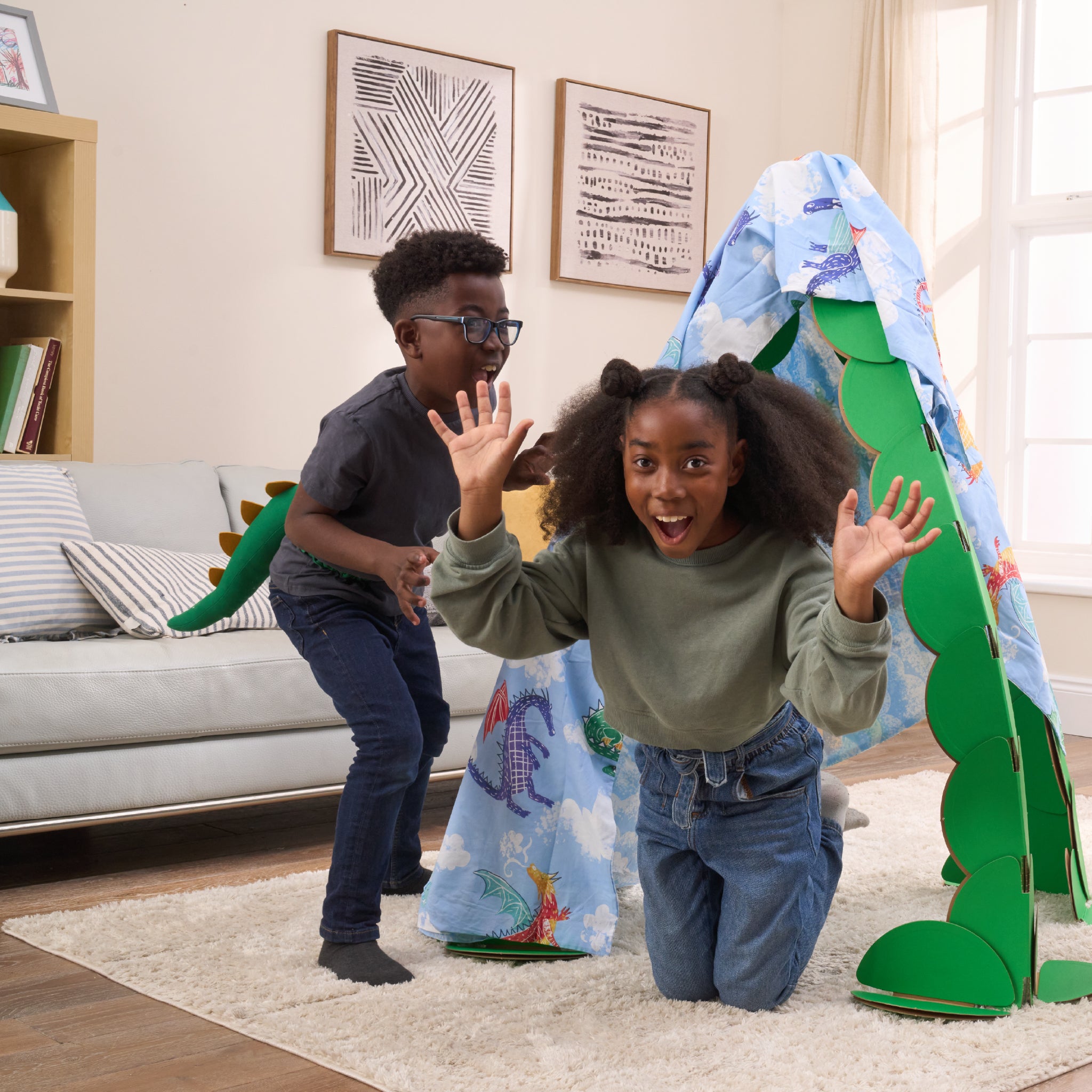 Three kids are playing in a living room, pretending to find dragons in a lair made out a noook play® building kit. The noook® den supports a sheet with dragons on.