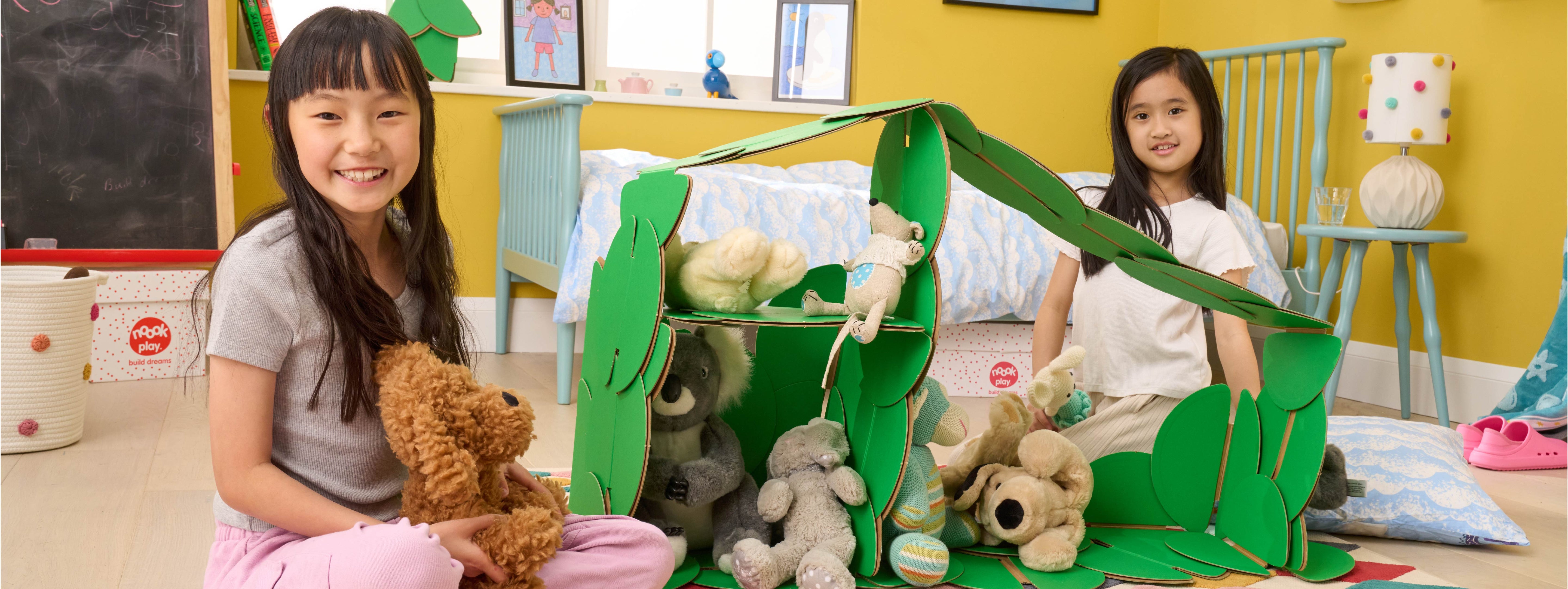 Two girls playing in a bedroom, with a dolls' house made out of a noook play® building kit.