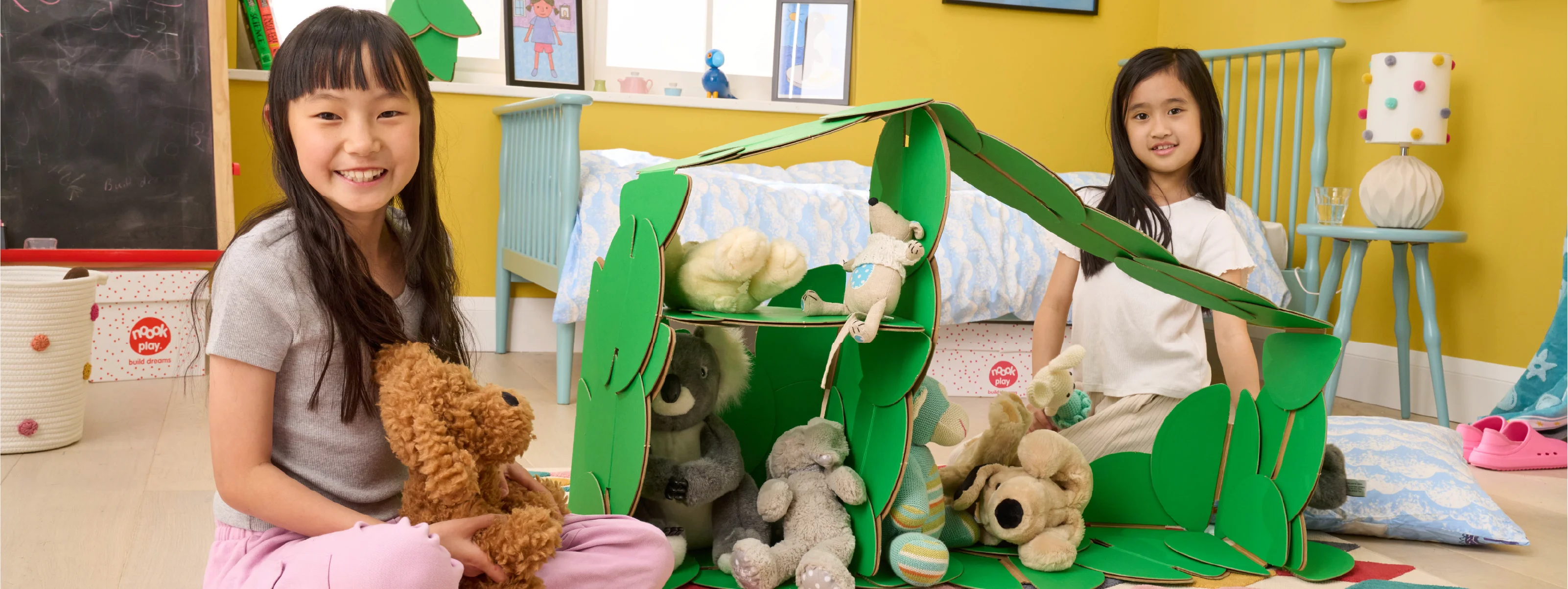 Two girls playing in a bedroom, with a dolls' house made out of a noook play® building kit.