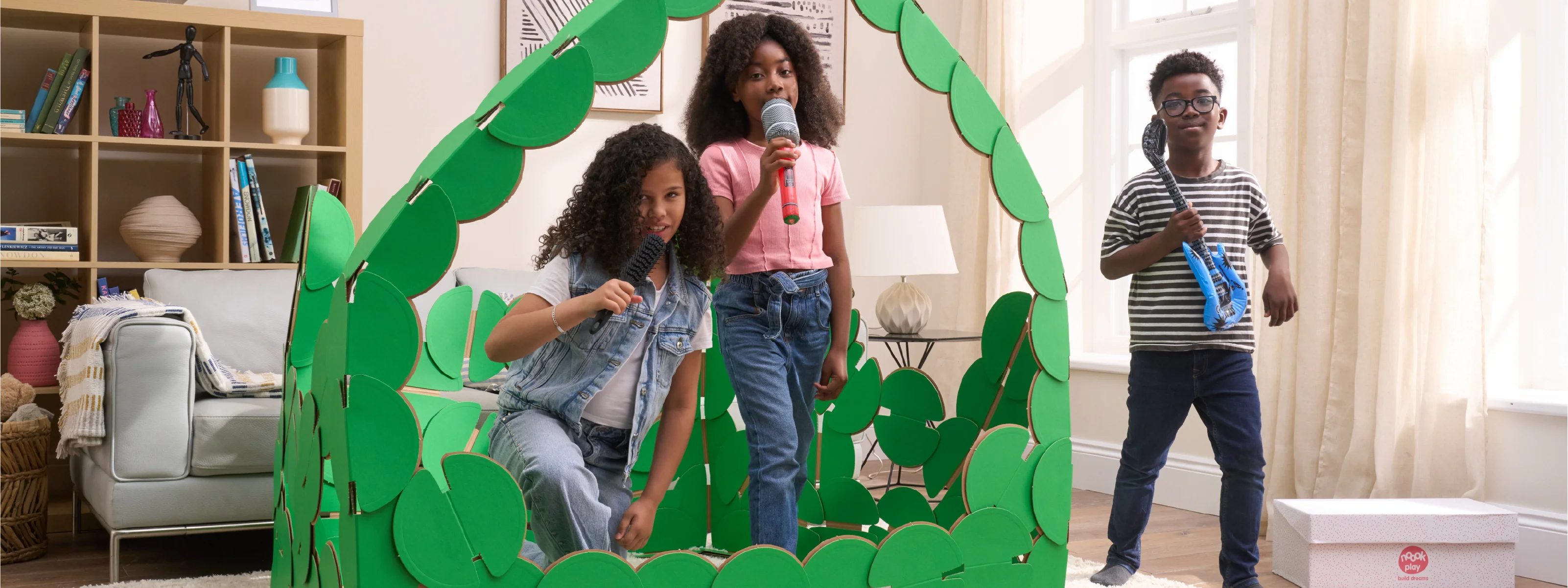 Three kids are playing in a sitting room, pretending to be pop singers on a concert stage made out of noook play® building kits. The girls are singing into microphones and the boy is strumming a blue inflatable guitar.
This Pop Stage took 85 noook play® discs to build.