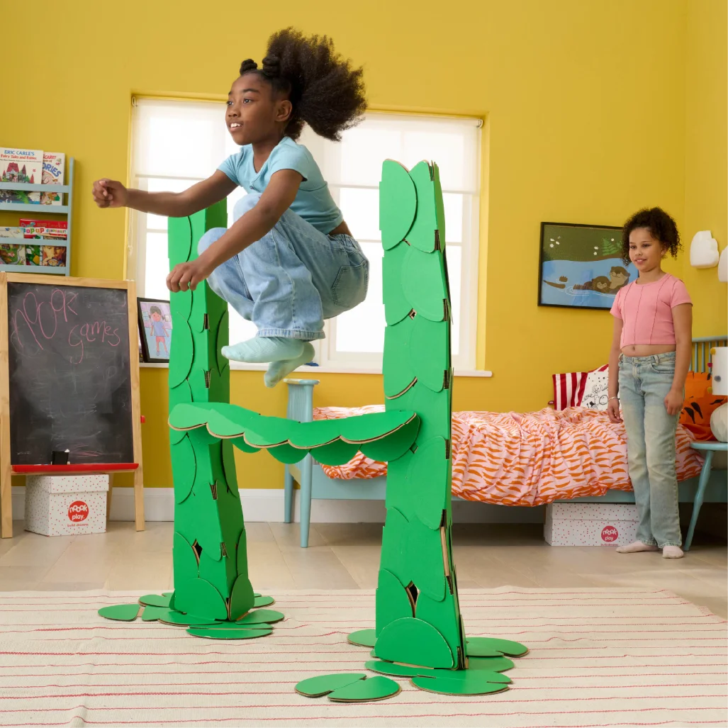 Two girls are playing in a bedroom, jumping over hurdles made out of a noook play® building kit.