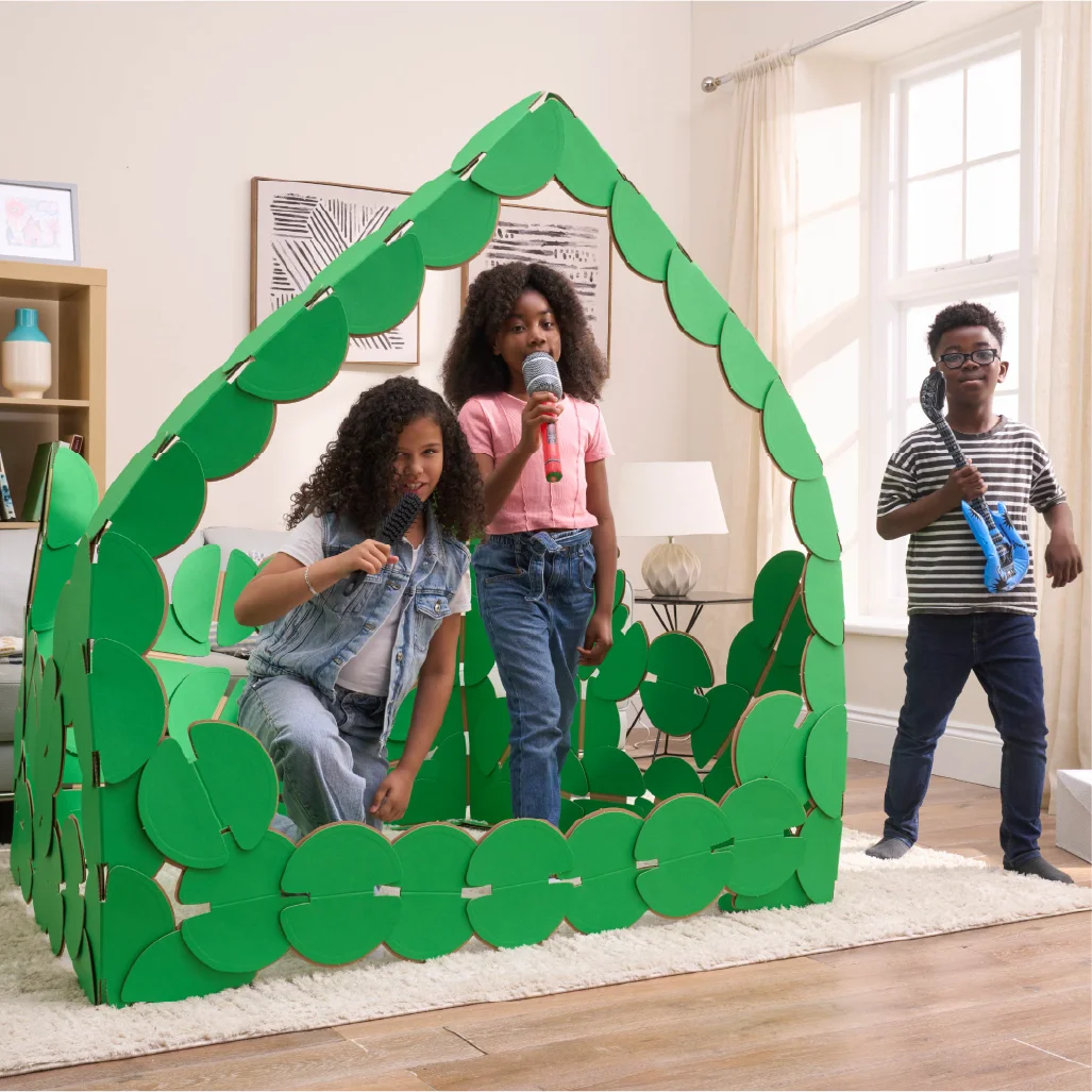 Three kids are playing in a sitting room, pretending to be pop singers on a concert stage made out of noook play® building kits. The girls are singing into microphones and the boy is strumming a blue inflatable guitar.
This Pop Stage took 85 noook play® discs to build.