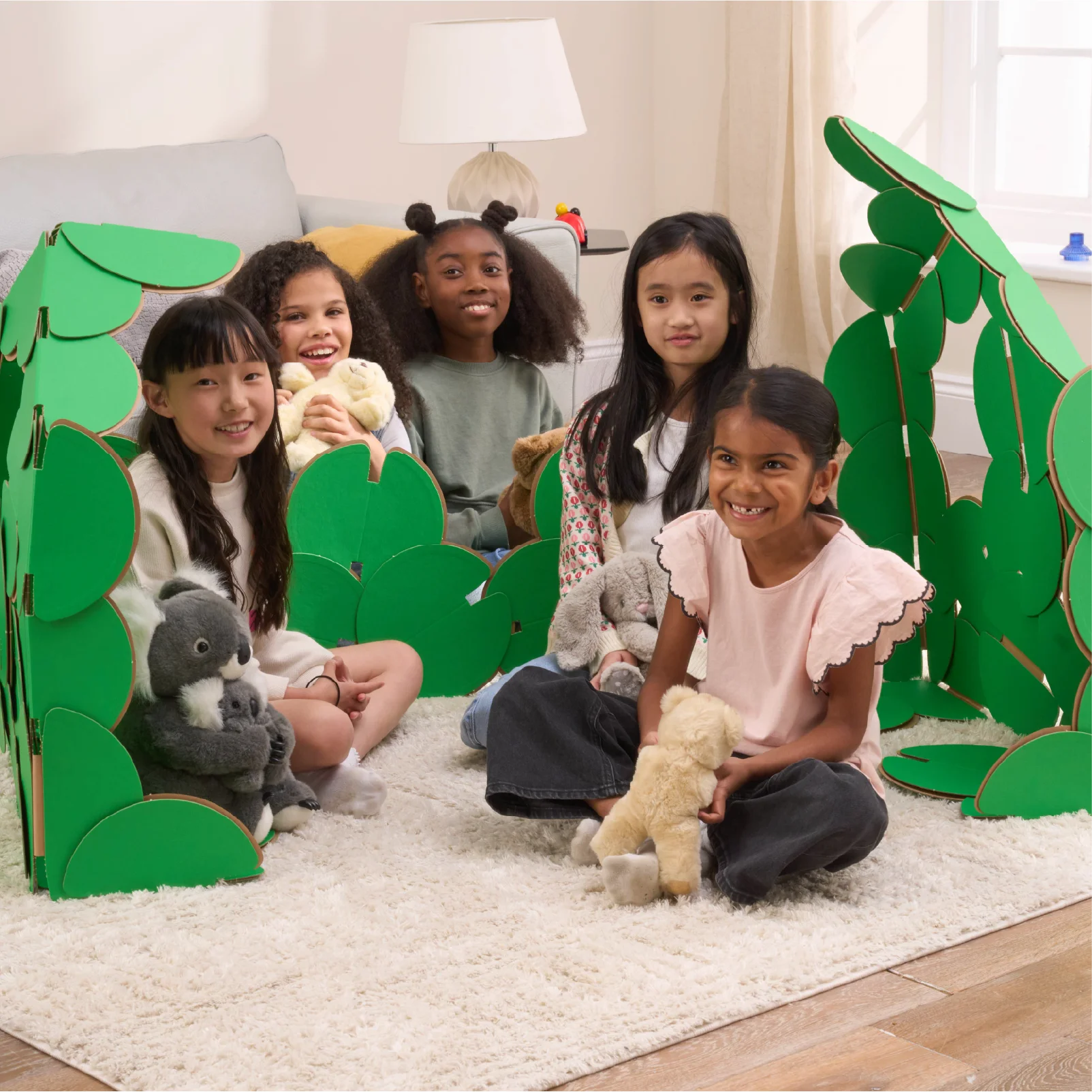 Five happy girls are having a party in a living room, with their teddies and a den made out of a noook play® building kit.