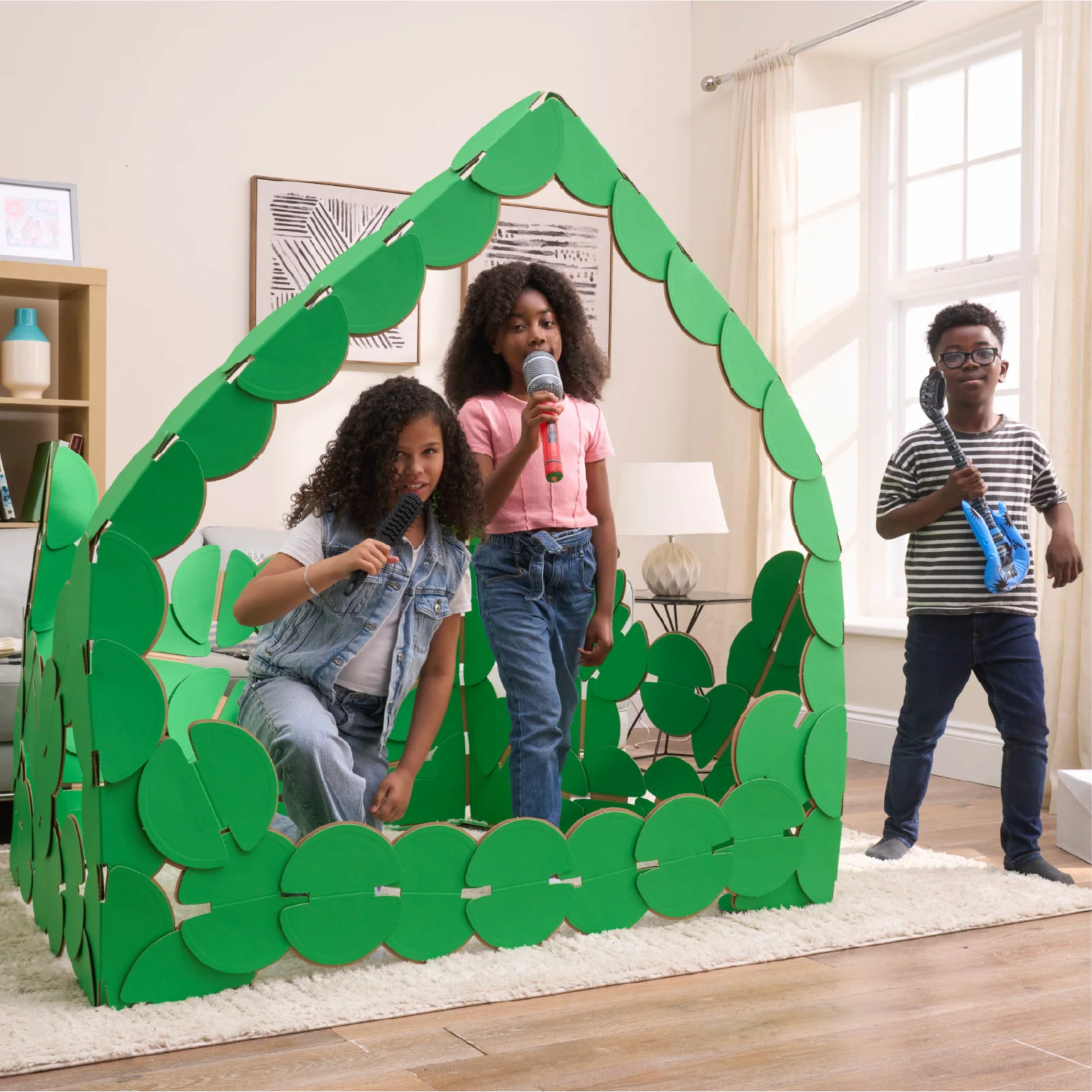 Three kids are playing in a sitting room, pretending to be pop singers on a concert stage made out of noook play® building kits. The girls are singing into microphones and the boy is strumming a blue inflatable guitar.
This Pop Stage took 85 noook play® discs to build.