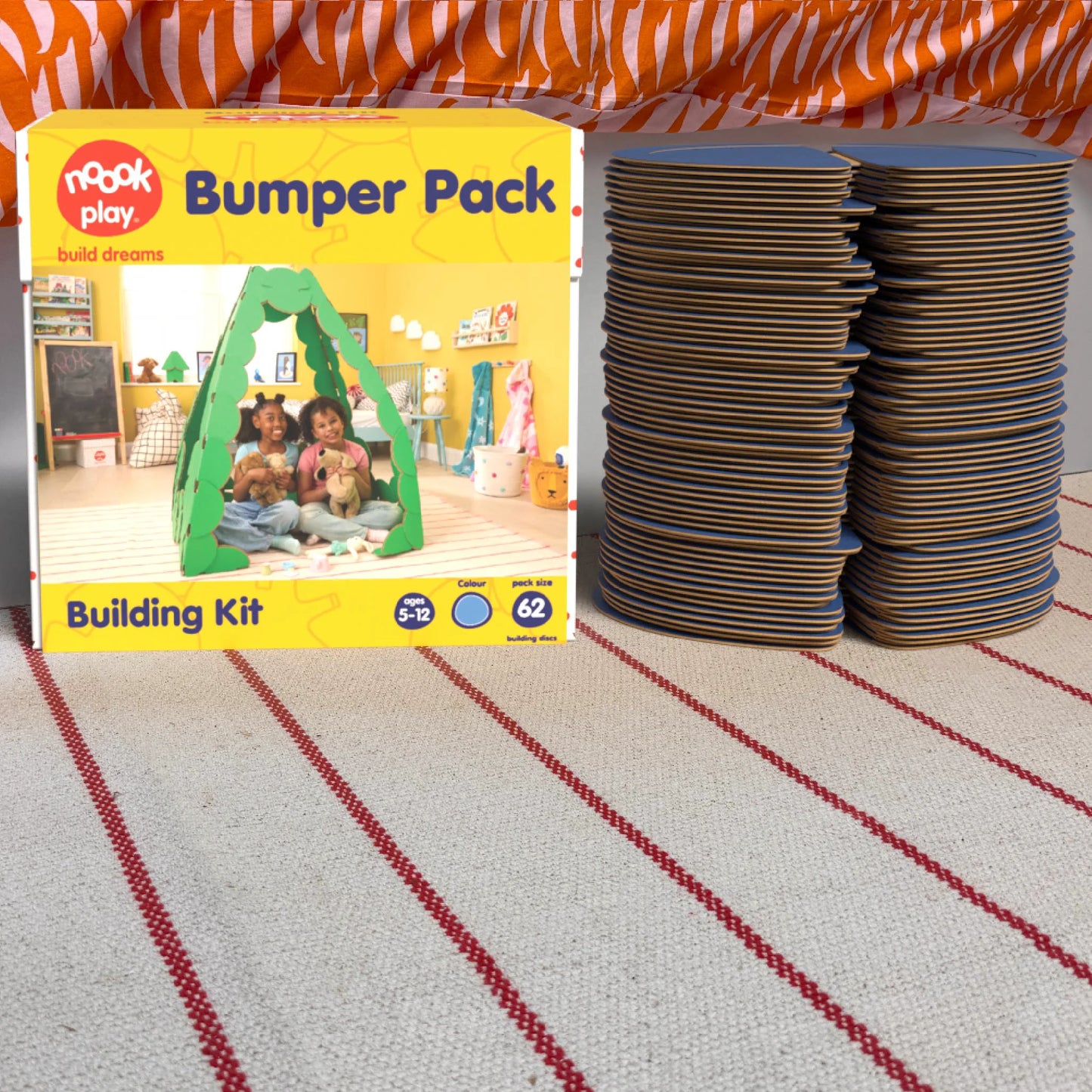 The noook play® Bumper Pack, 62 Pieces, in blue, shown at the foot of a child bed, on a stripy rug
