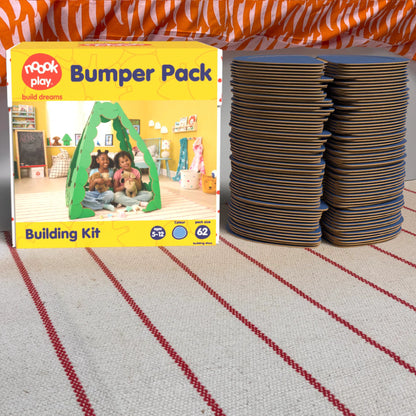 The noook play® Bumper Pack, 62 Pieces, in blue, shown at the foot of a child bed, on a stripy rug