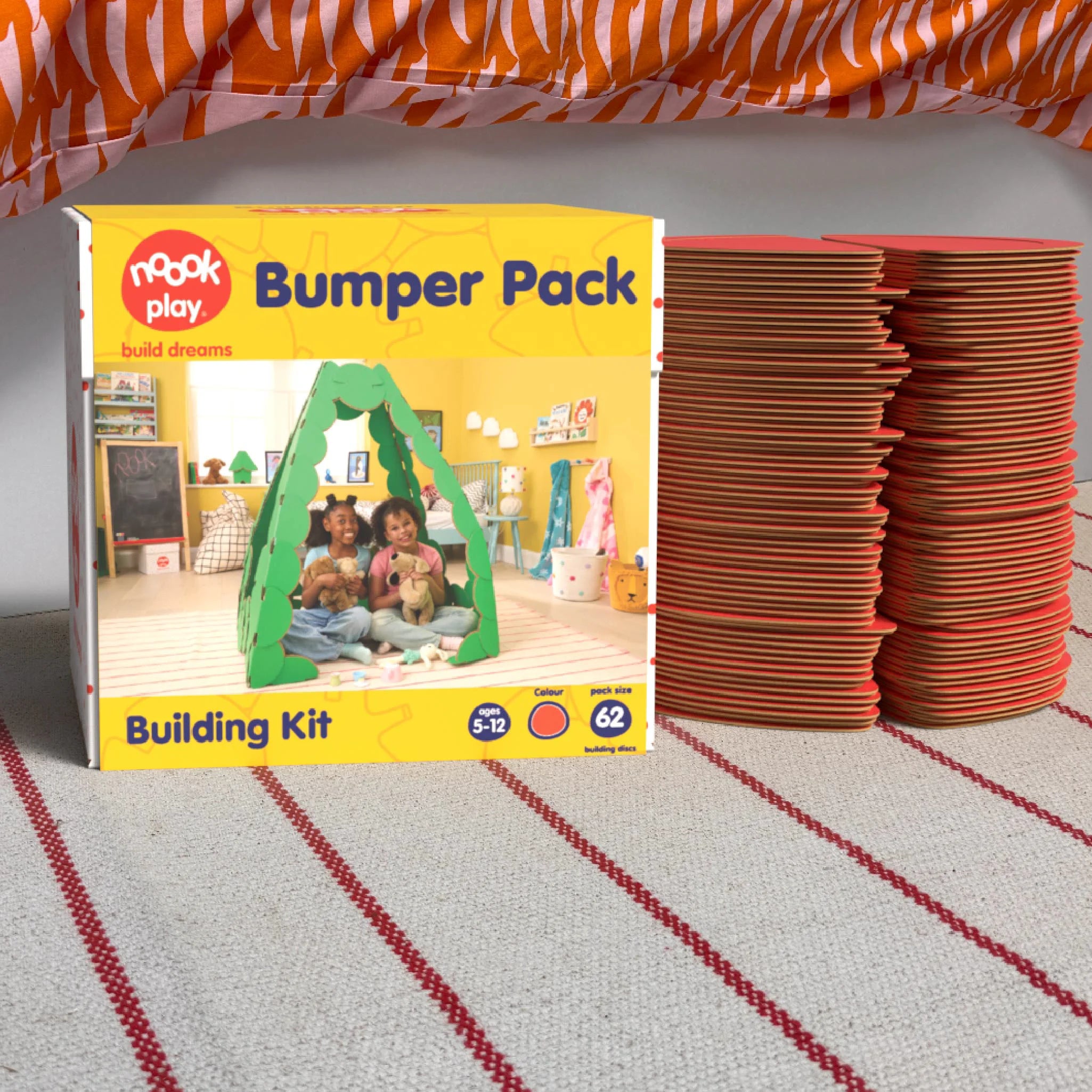 The noook play® Bumper Pack, 62 Pieces, in red, shown at the foot of a child bed, on a stripy rug