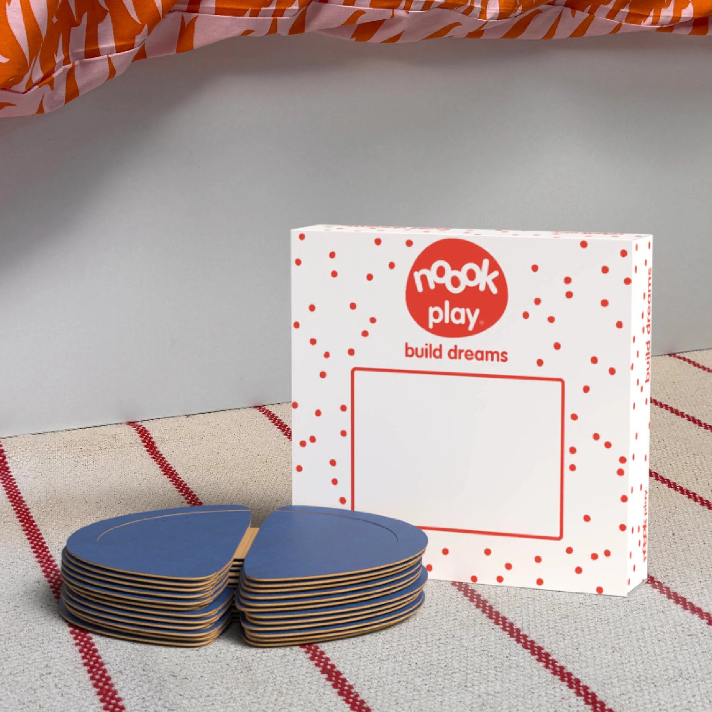 The noook play® Expansion Pack, 12 Pieces, in blue, shown at the foot of a child bed, on a stripy rug