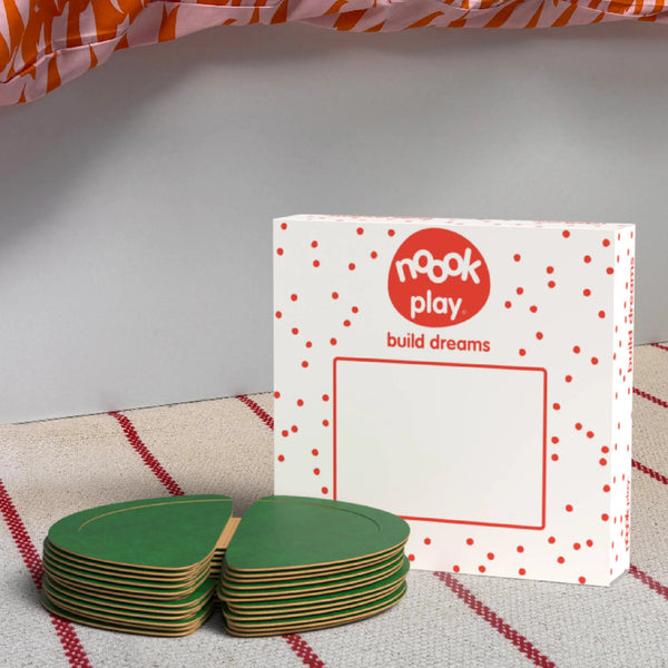 The noook play® Expansion Pack, 12 Pieces, in green, shown at the foot of a child bed, on a stripy rug