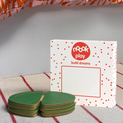 The noook play® Expansion Pack, 12 Pieces, in green, shown at the foot of a child bed, on a stripy rug