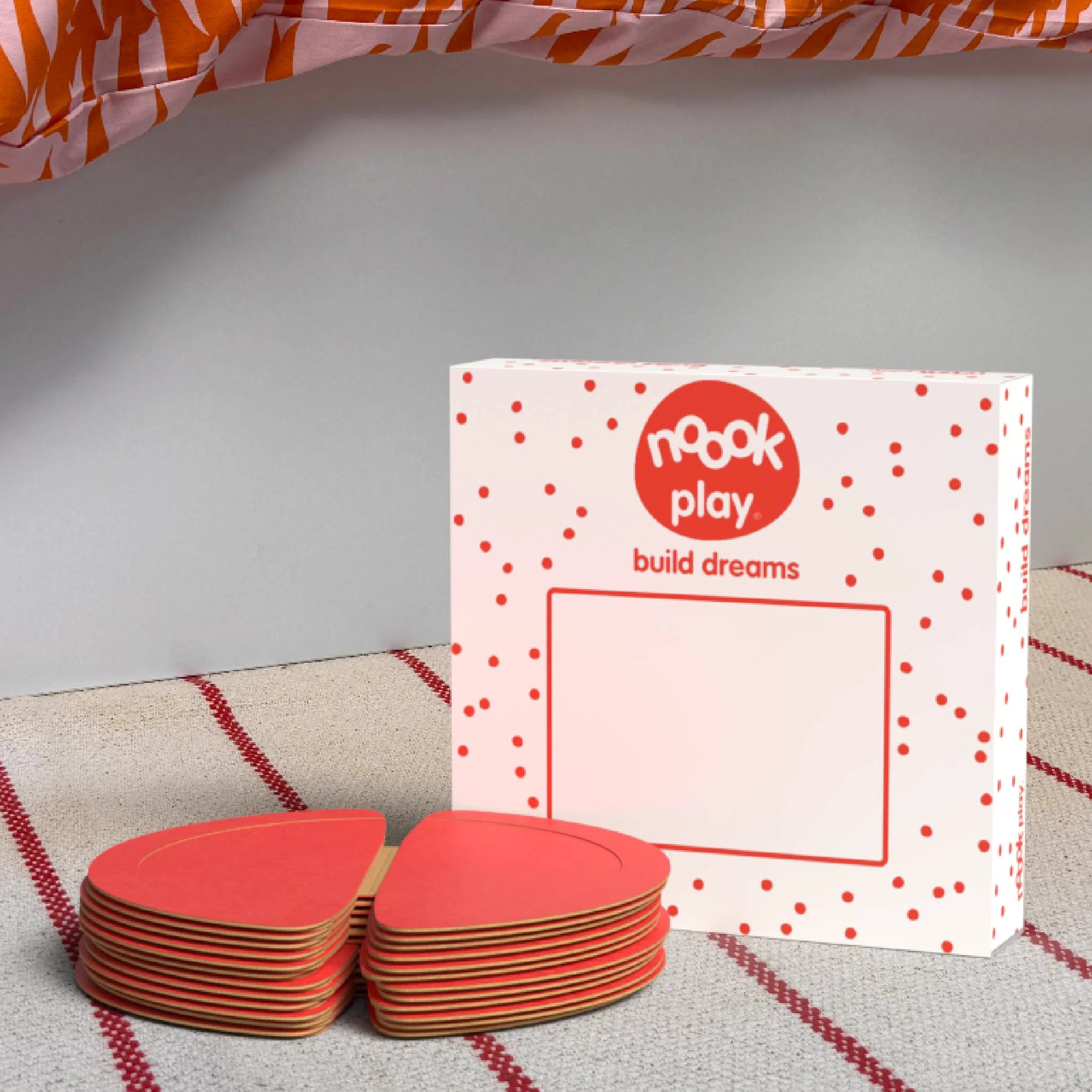 The noook play® Expansion Pack, 12 Pieces, in red, shown at the foot of a child bed, on a stripy rug
