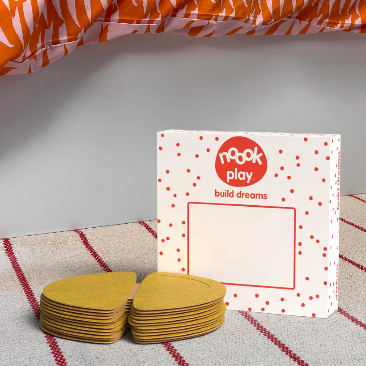 The noook play® Expansion Pack, 12 Pieces, in yellow, shown at the foot of a child bed, on a stripy rug