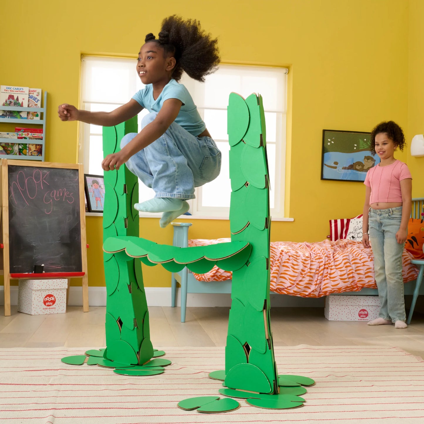 Two girls are playing in a bedroom, jumping over hurdles made out of a noook play® building kit.