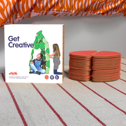 The noook play® Starter Pack, 30 Pieces, in red, shown at the foot of a child bed, on a stripy rug