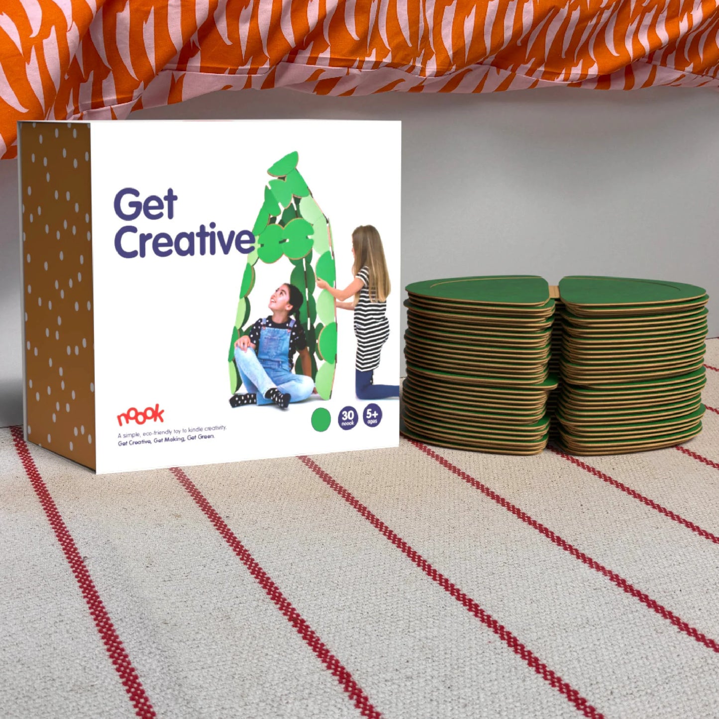 The noook play® Starter Pack, 30 Pieces, in green, shown at the foot of a child bed, on a stripy rug