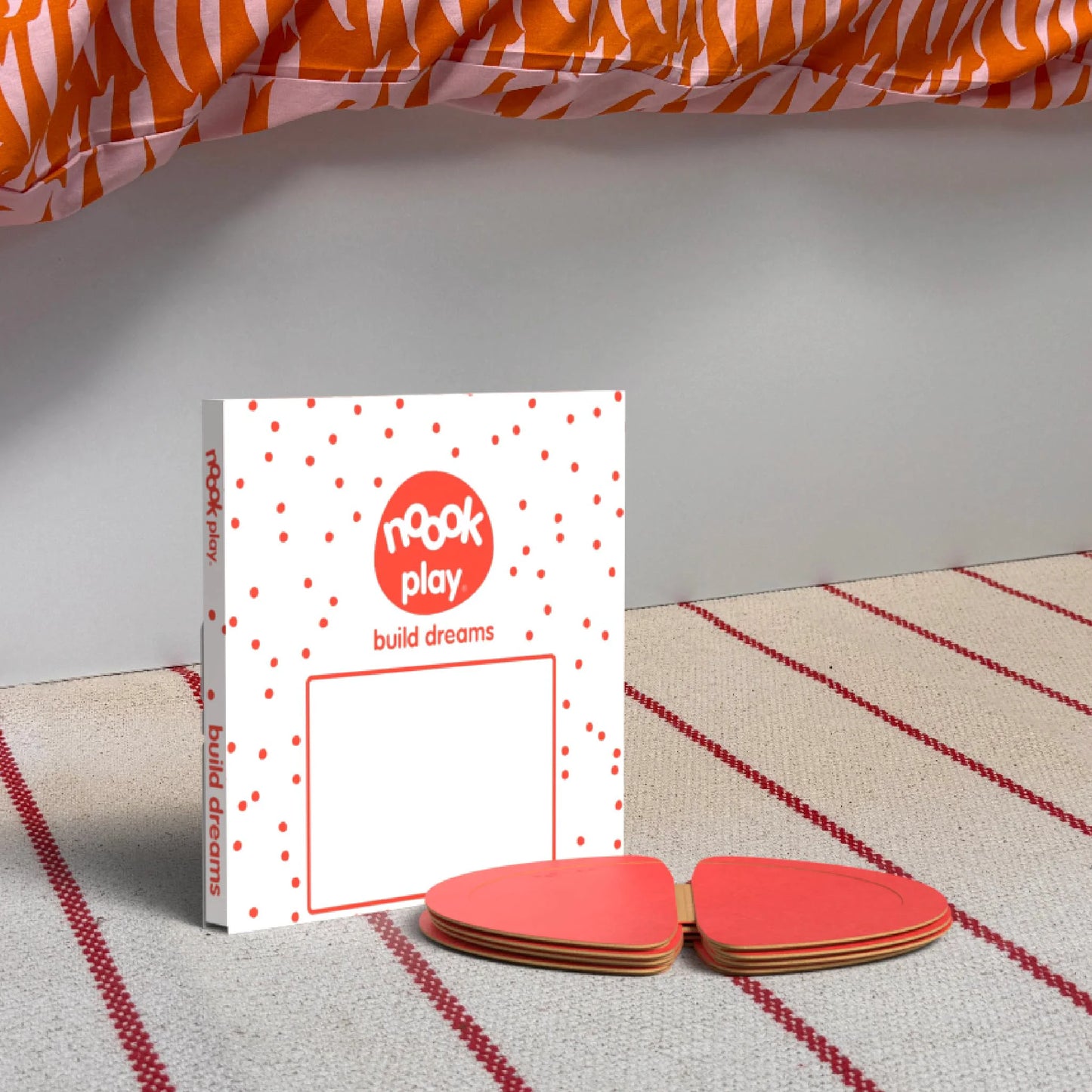 The noook play® Top-Up Pack, 12 Pieces, in red, shown at the foot of a child bed, on a stripy rug