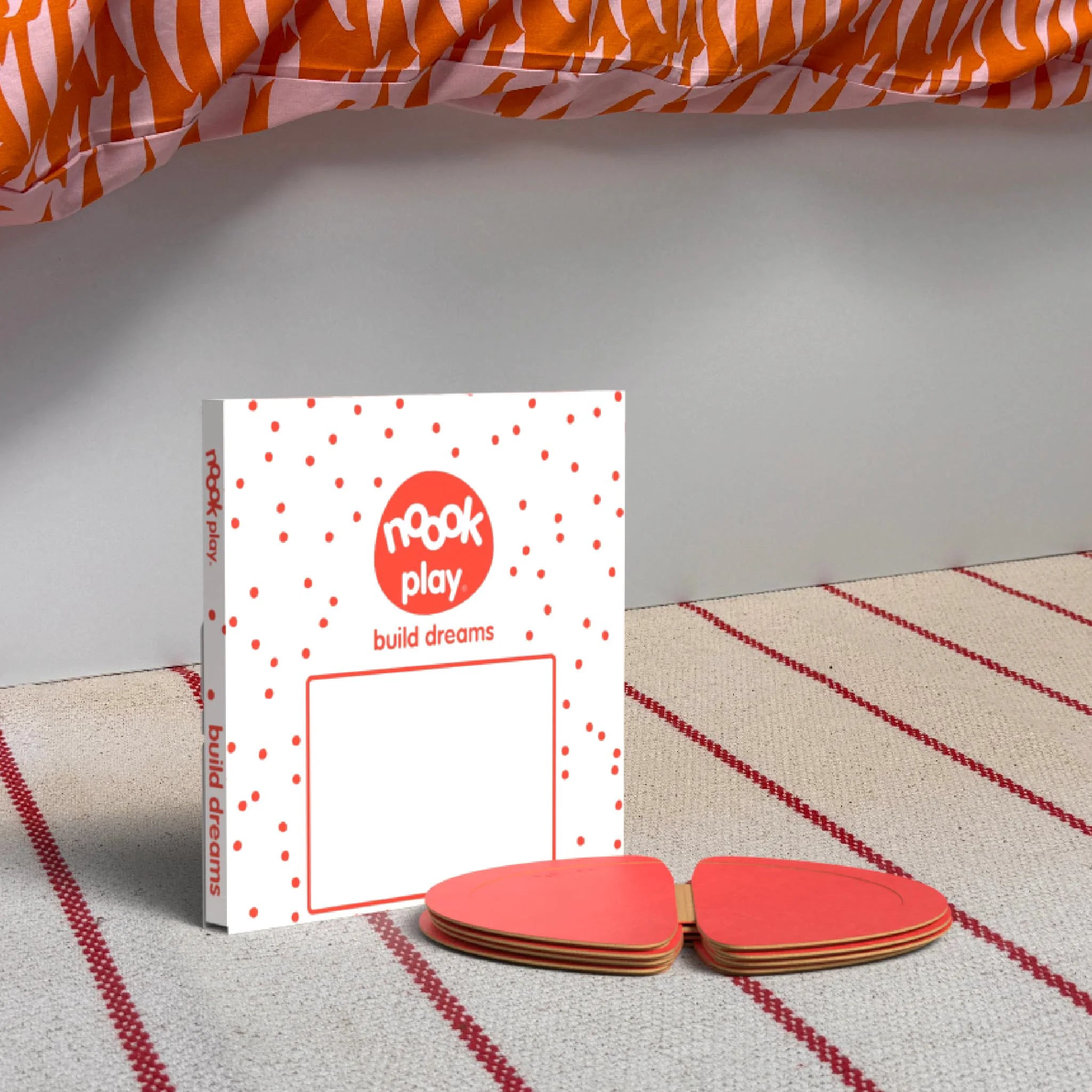 The noook play® Top-Up Pack, 12 Pieces, in red, shown at the foot of a child bed, on a stripy rug