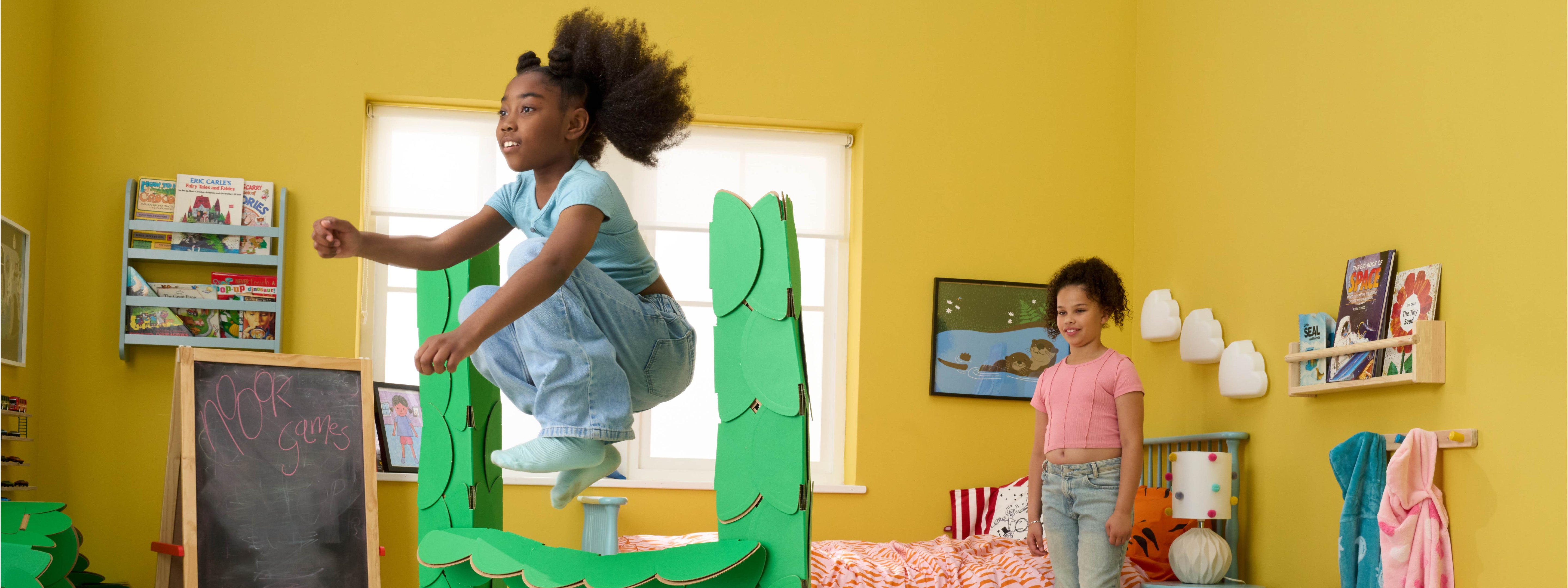 Two girls are playing in a bedroom, jumping over hurdles made out of a noook play® building kit.