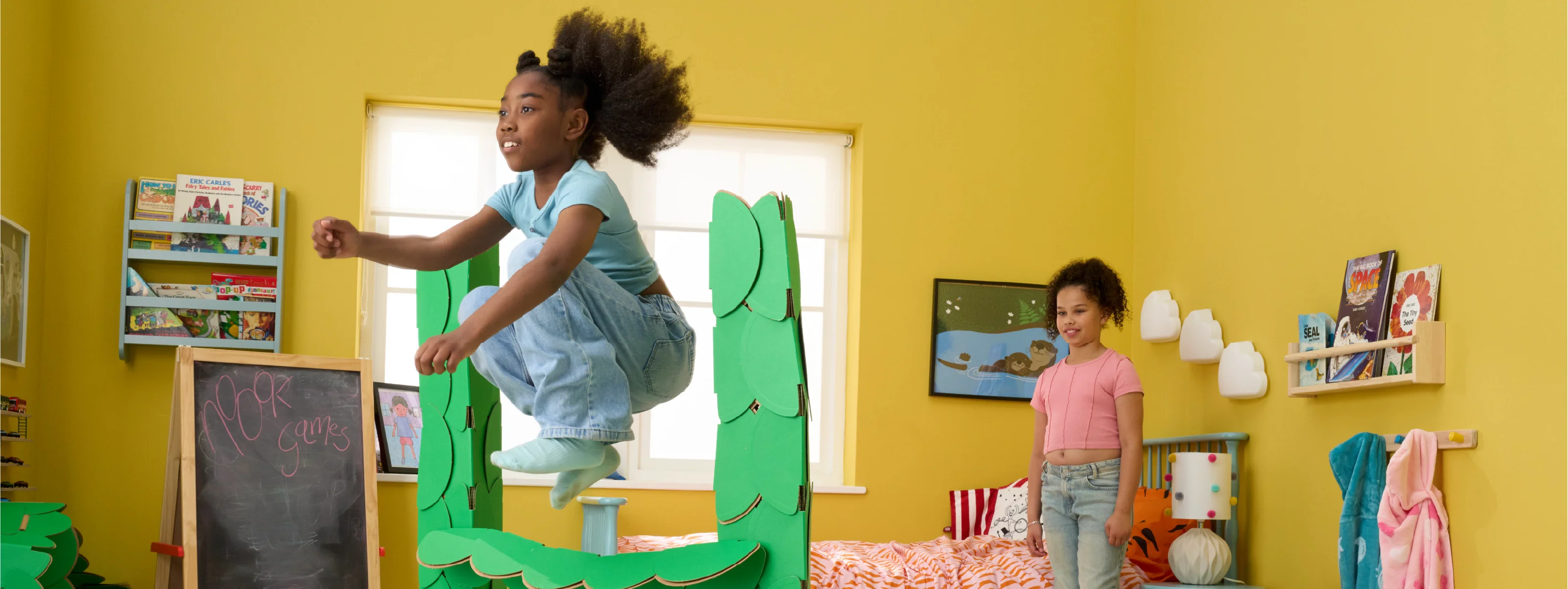 Two girls are playing in a bedroom, jumping over hurdles made out of a noook play® building kit.
