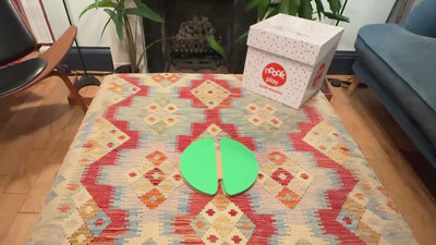 A pair of hands demonstrates how to use noook play discs. The hands slide two large circular green discs together using the slots in each piece. The discs lock in place through friction, then are gently pulled apart to show how easily they disconnect. The hands repeat the action in different directions to show that the discs can connect at multiple angles. The background is a clean, well-lit surface with no other objects.